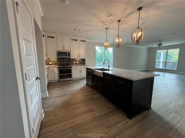 kitchen featuring a kitchen island with sink, white cabinets, ceiling fan with notable chandelier, wood-type flooring, and stainless steel appliances