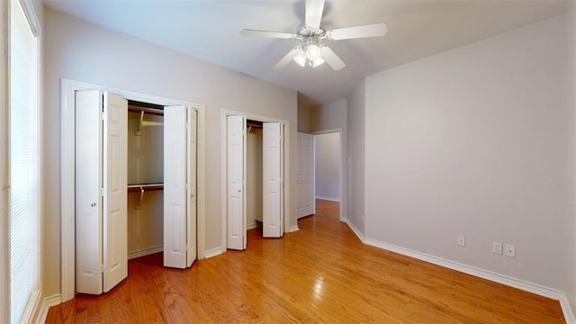 unfurnished bedroom with light wood-type flooring, ceiling fan, baseboards, and two closets