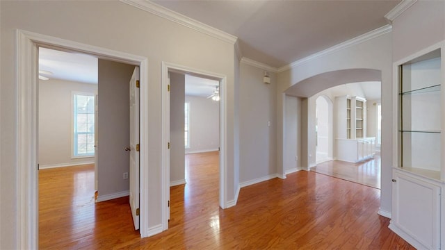 interior space featuring light wood-type flooring, baseboards, arched walkways, and ornamental molding