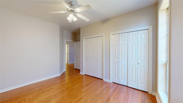 unfurnished bedroom with light wood-type flooring, ceiling fan, baseboards, and two closets