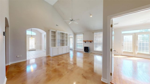 unfurnished living room featuring arched walkways, high vaulted ceiling, a wealth of natural light, and a ceiling fan