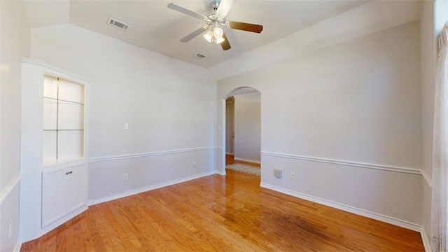 spare room featuring visible vents, baseboards, ceiling fan, light wood-type flooring, and arched walkways