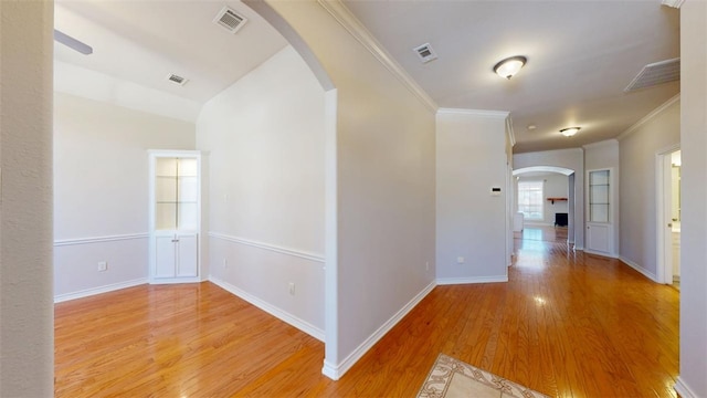 hall featuring arched walkways, visible vents, crown molding, and light wood finished floors