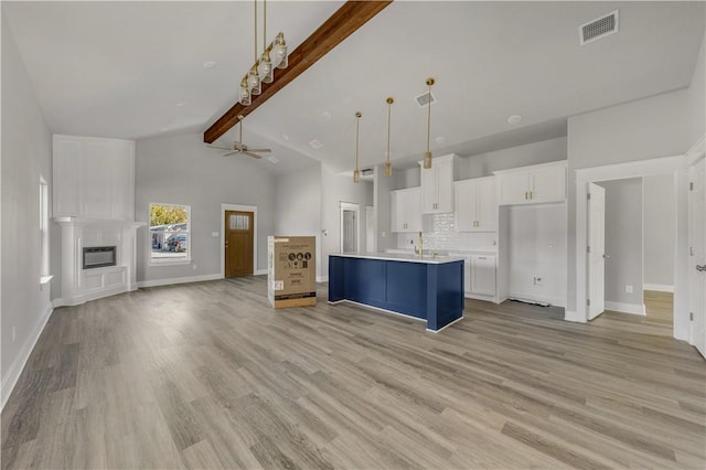 kitchen with beamed ceiling, decorative light fixtures, a center island with sink, white cabinets, and light wood-type flooring