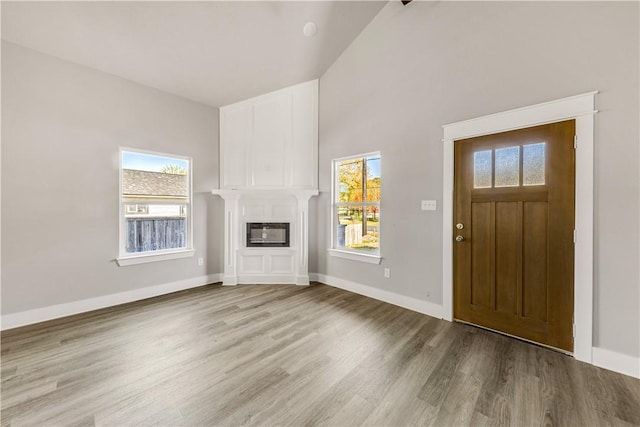 foyer entrance featuring light wood-type flooring, a fireplace, high vaulted ceiling, and heating unit