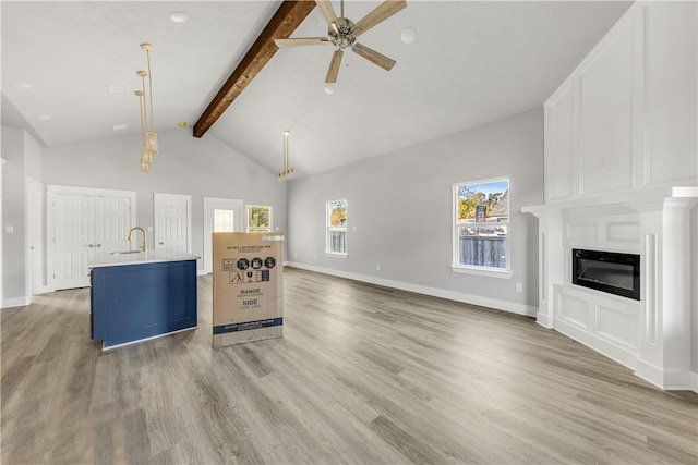 unfurnished living room featuring beam ceiling, ceiling fan, a healthy amount of sunlight, and light wood-type flooring