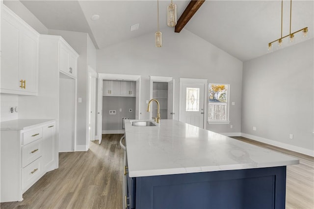 kitchen with beam ceiling, sink, decorative light fixtures, and an island with sink