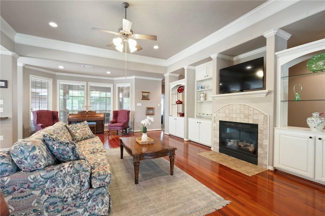 living area with crown molding, ceiling fan, wood finished floors, and a tile fireplace