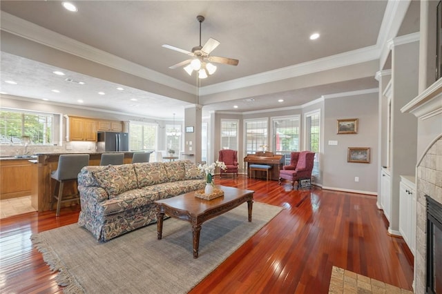 living area featuring plenty of natural light, wood-type flooring, a ceiling fan, and a tile fireplace