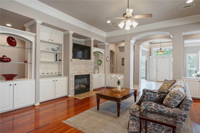 living area with crown molding, a tiled fireplace, a ceiling fan, wood finished floors, and visible vents