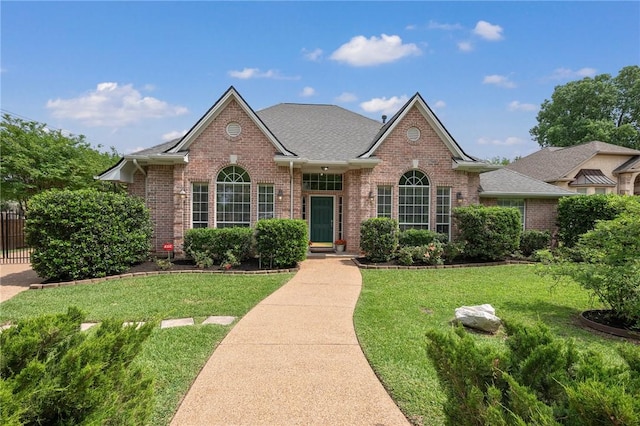 ranch-style home featuring brick siding, fence, a shingled roof, and a front yard