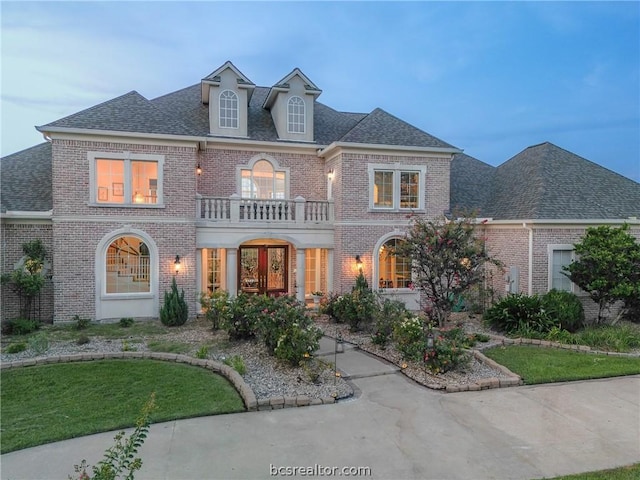 colonial inspired home with a balcony, roof with shingles, and brick siding