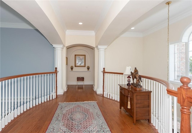 corridor featuring an upstairs landing, wood finished floors, decorative columns, and crown molding