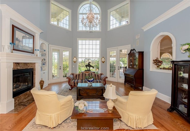 living room with french doors, light hardwood / wood-style flooring, a towering ceiling, a fireplace, and a chandelier