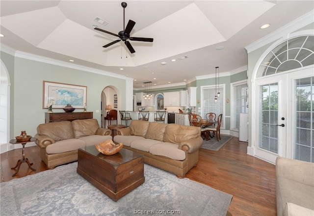 living area featuring arched walkways, wood finished floors, a raised ceiling, and visible vents