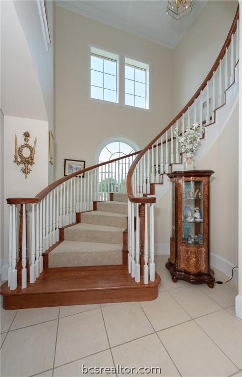 stairway featuring tile patterned flooring, crown molding, a towering ceiling, and baseboards