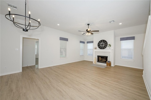 unfurnished living room with plenty of natural light, a tile fireplace, ceiling fan with notable chandelier, and light hardwood / wood-style flooring