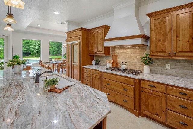 3281 Toltec Trl, College Station, TX 77845 - kitchen featuring stainless steel gas cooktop, light stone countertops, premium range hood, brown cabinets, and a sink