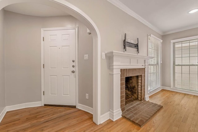 entryway with a brick fireplace, wood-type flooring, and ornamental molding