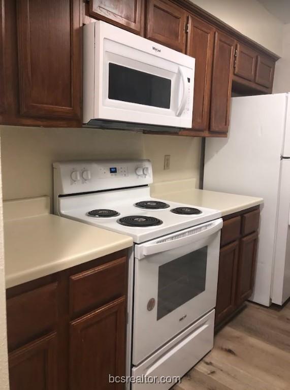 kitchen with dark brown cabinets, light wood-type flooring, and white appliances