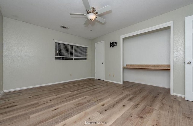 unfurnished bedroom featuring ceiling fan, light hardwood / wood-style floors, built in desk, and a closet