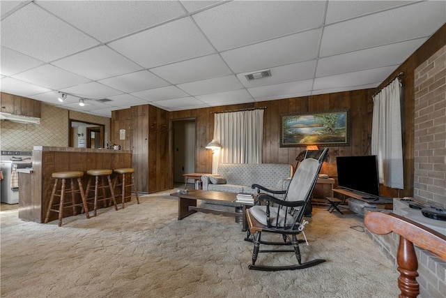 carpeted living room featuring bar, a drop ceiling, brick wall, and wooden walls