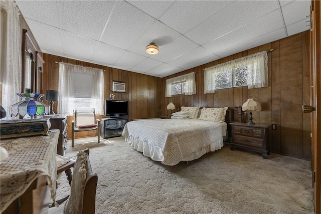 carpeted bedroom featuring a paneled ceiling, wood walls, and a wall mounted air conditioner