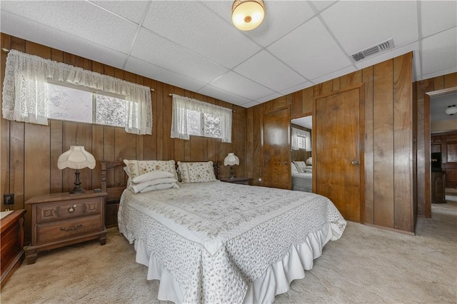 carpeted bedroom with a paneled ceiling, wood walls, and a closet