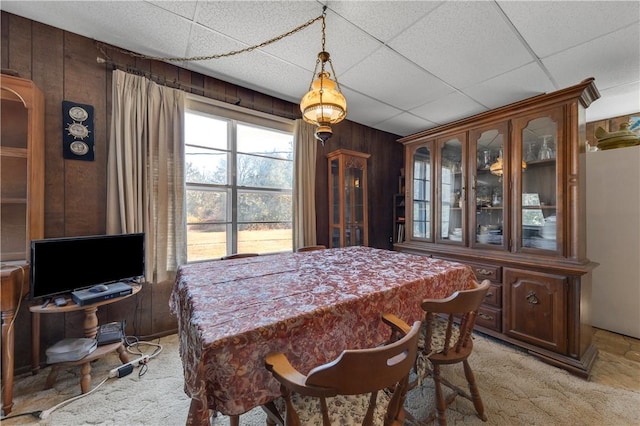 dining space with a paneled ceiling, wood walls, and light colored carpet