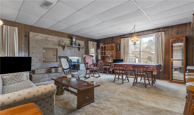 living room featuring a paneled ceiling, wooden walls, and light carpet