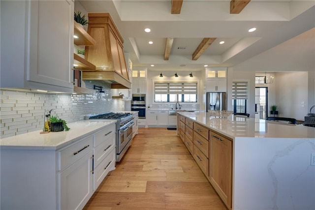 kitchen with a spacious island, beam ceiling, white cabinets, and appliances with stainless steel finishes