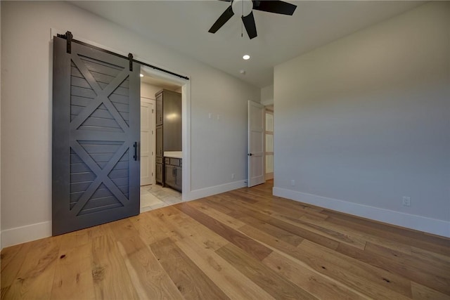 empty room with ceiling fan, a barn door, and light hardwood / wood-style flooring