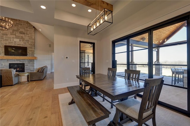 dining room with a towering ceiling, a stone fireplace, a chandelier, and light wood-type flooring