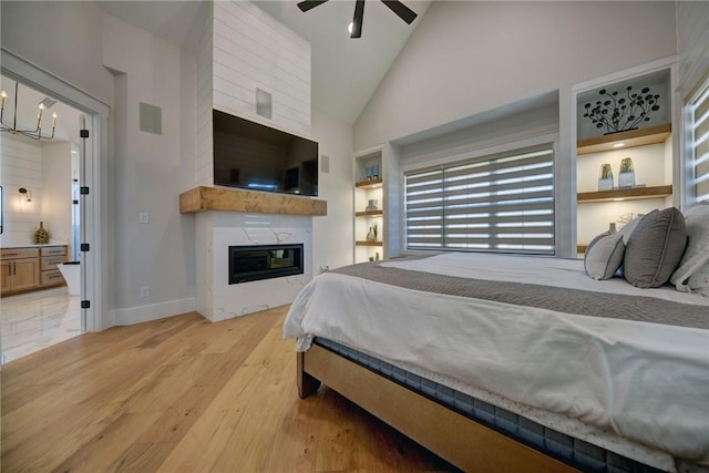 bedroom featuring ceiling fan with notable chandelier, connected bathroom, high vaulted ceiling, a large fireplace, and light wood-type flooring