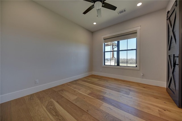 unfurnished room featuring a barn door, ceiling fan, and light wood-type flooring