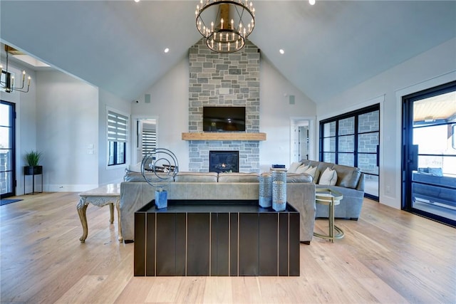 living room with an inviting chandelier, a stone fireplace, high vaulted ceiling, and light hardwood / wood-style floors