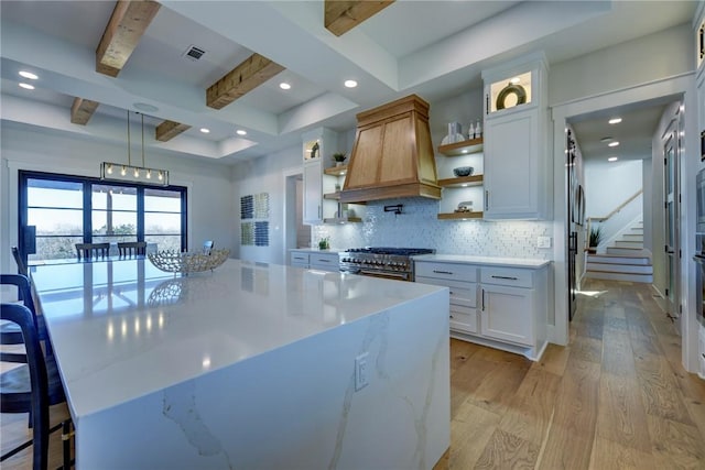 kitchen with premium range hood, white cabinetry, backsplash, double oven range, and light hardwood / wood-style floors