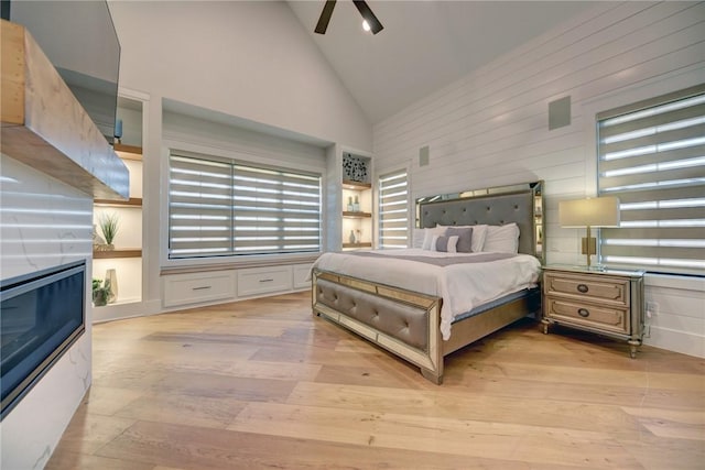 bedroom featuring ceiling fan, high vaulted ceiling, wooden walls, and light hardwood / wood-style flooring