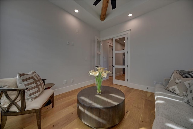 living area featuring beam ceiling, ceiling fan, and light wood-type flooring