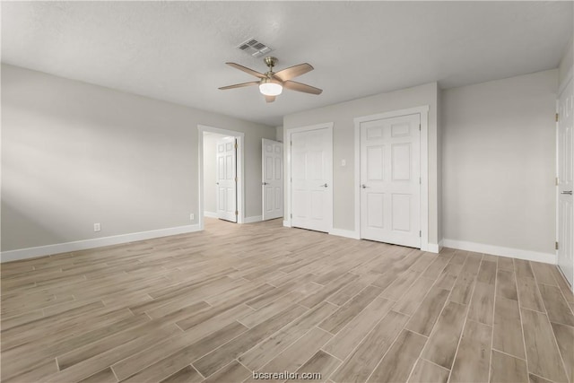 unfurnished bedroom with two closets, light hardwood / wood-style flooring, and ceiling fan