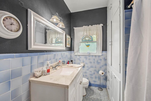 full bathroom with tile walls, vanity, toilet, and a wainscoted wall