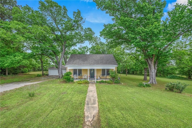 view of front of house with a porch, a front lawn, a detached garage, and view of wooded area