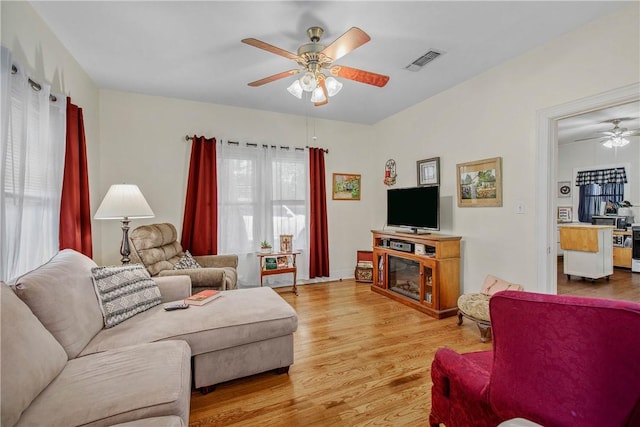 living area with a ceiling fan, light wood-style flooring, a glass covered fireplace, and healthy amount of natural light