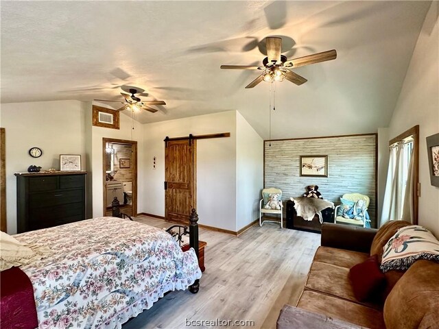 bedroom featuring a barn door, ceiling fan, light hardwood / wood-style flooring, and vaulted ceiling