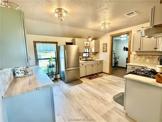 kitchen featuring tasteful backsplash, a textured ceiling, stainless steel refrigerator, and light hardwood / wood-style flooring