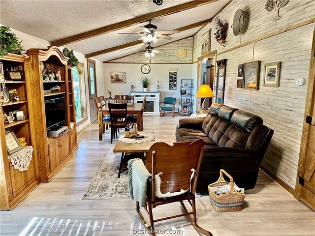 living room with vaulted ceiling with beams, ceiling fan, wooden walls, and light hardwood / wood-style flooring