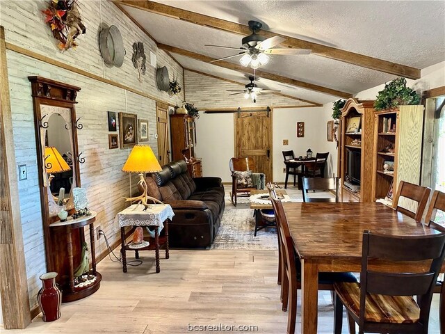 dining room featuring beam ceiling, a barn door, light hardwood / wood-style flooring, wood walls, and a textured ceiling