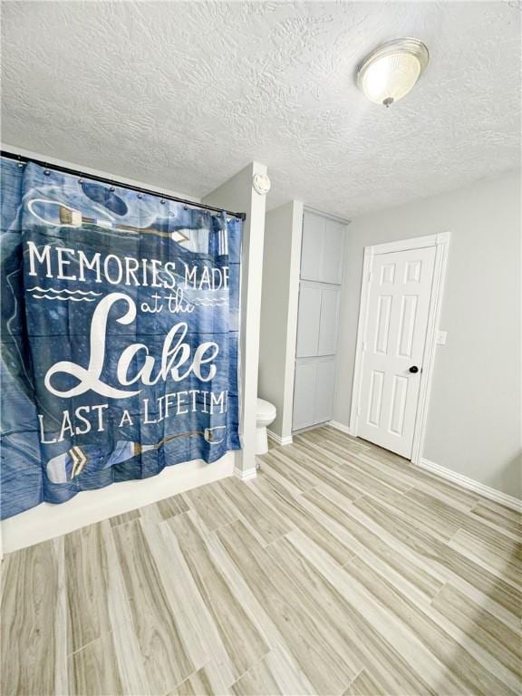 9462 Riley Green Rd, Franklin, TX 77856 - full bathroom featuring wood finished floors, baseboards, shower / bath combination with curtain, a textured ceiling, and toilet