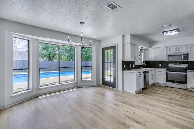 kitchen featuring a sink, a textured ceiling, light wood finished floors, appliances with stainless steel finishes, and visible vents