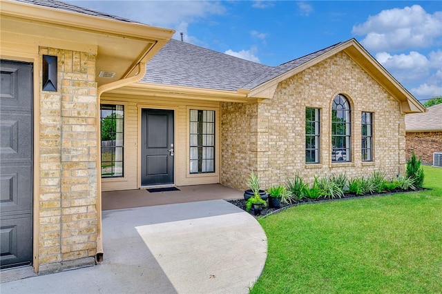 entrance to property with a lawn, roof with shingles, and brick siding